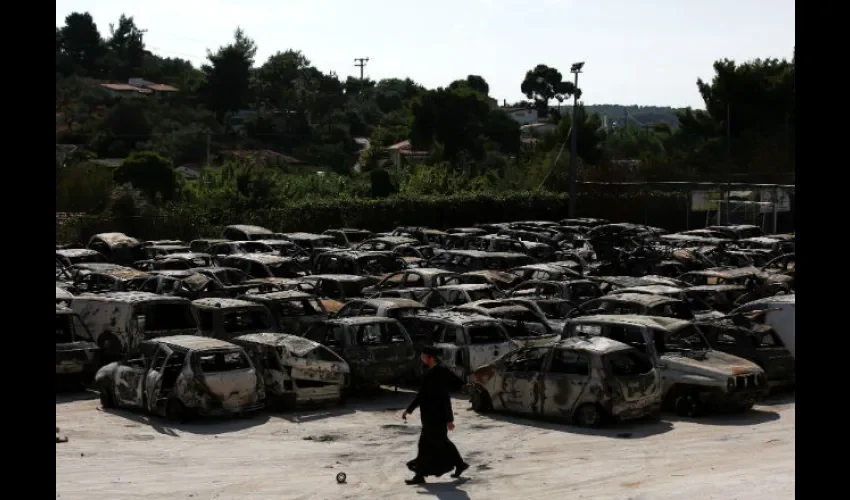 Un sacerdote ortodoxo camina frente a coches calcinados tras el incendio forestal. Foto: EFE